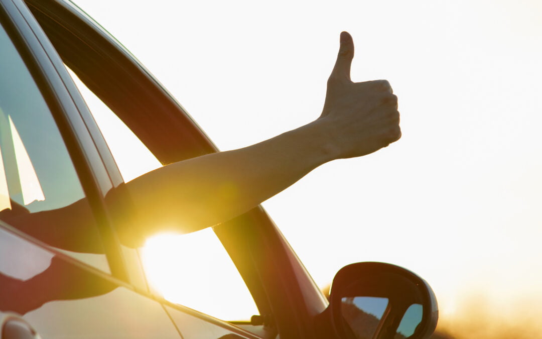 Man showing thumbs up from car window at sunset. Vacation and travel concept - great driving habits