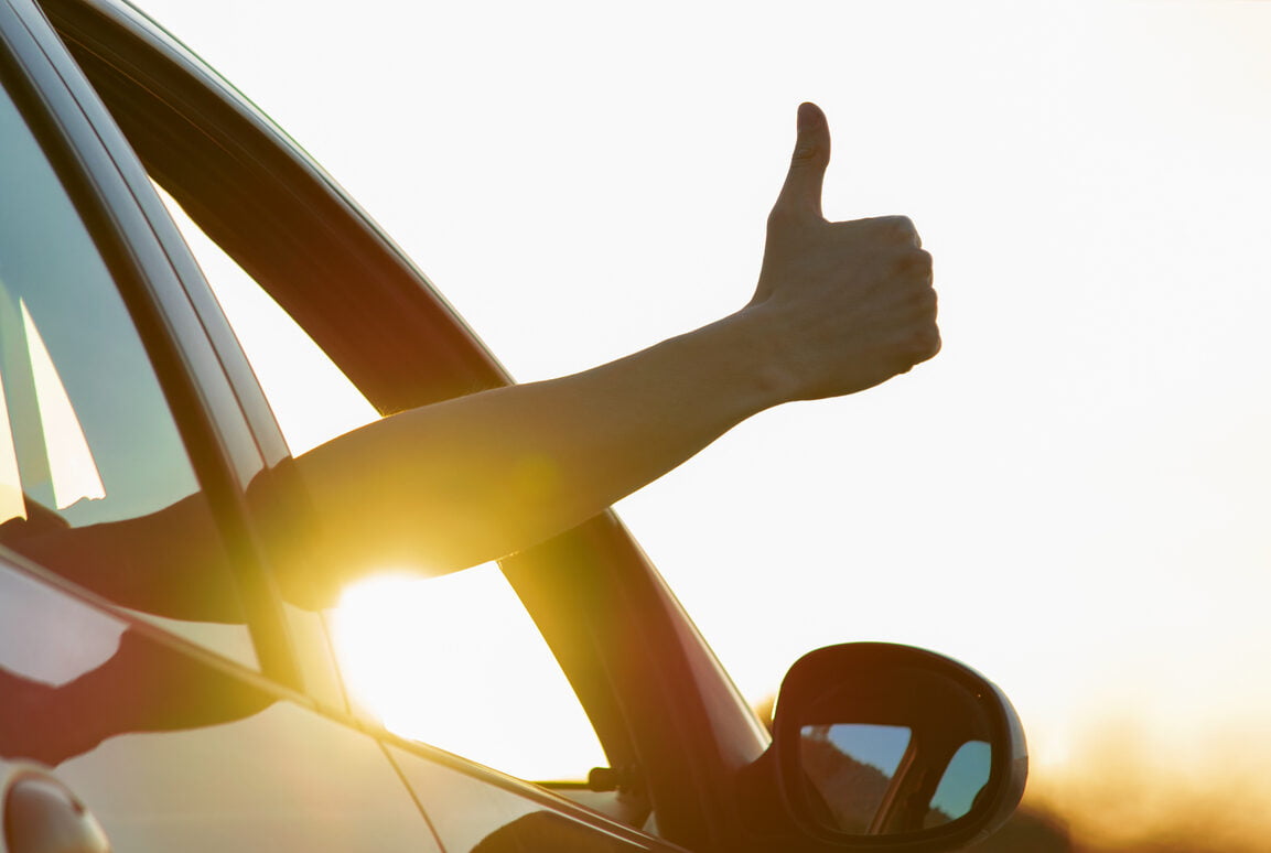 Man showing thumbs up from car window at sunset. Vacation and travel concept - great driving habits