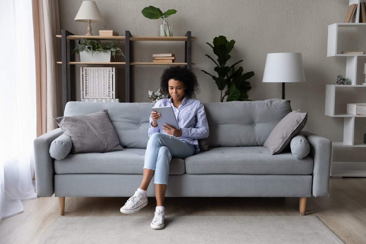 Young African American woman sit relax on couch at home use modern tablet gadget browse internet. Millennial biracial female rest on sofa talk speak on video webcam call on pad device online - renter's checklist