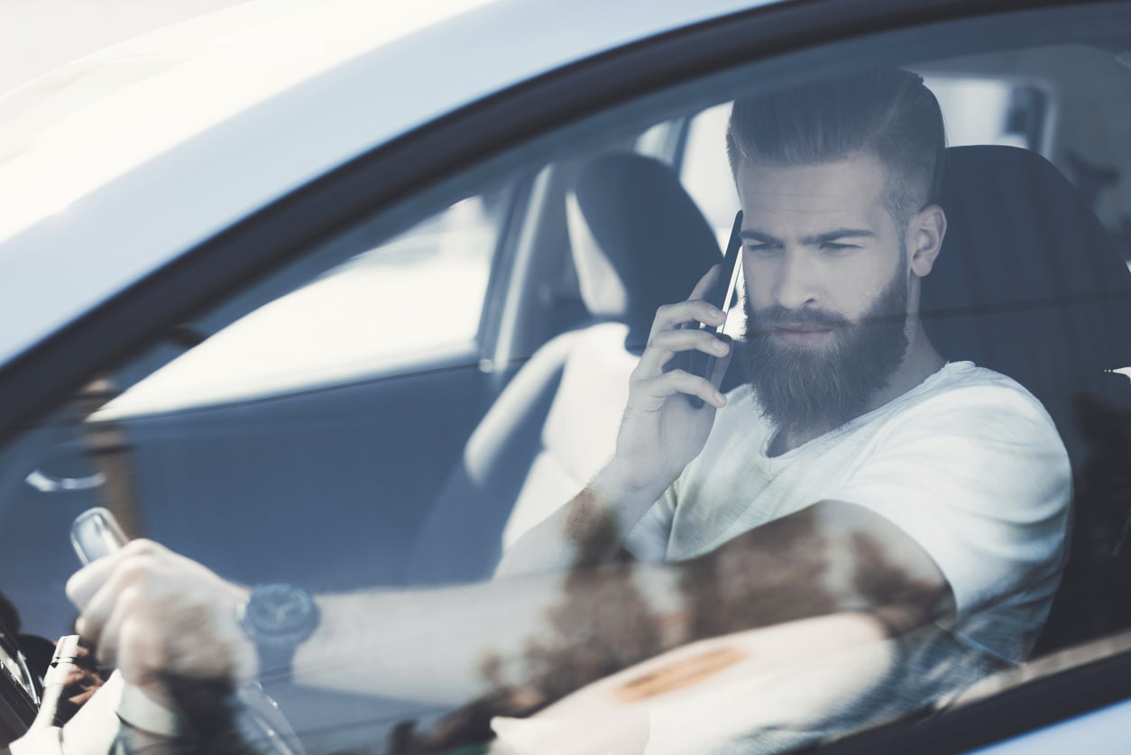 distracted driving charges - A young man with a beard sits at the wheel of an electric vehicle. He is focused on the road. He feels confident in the cabin of this car.