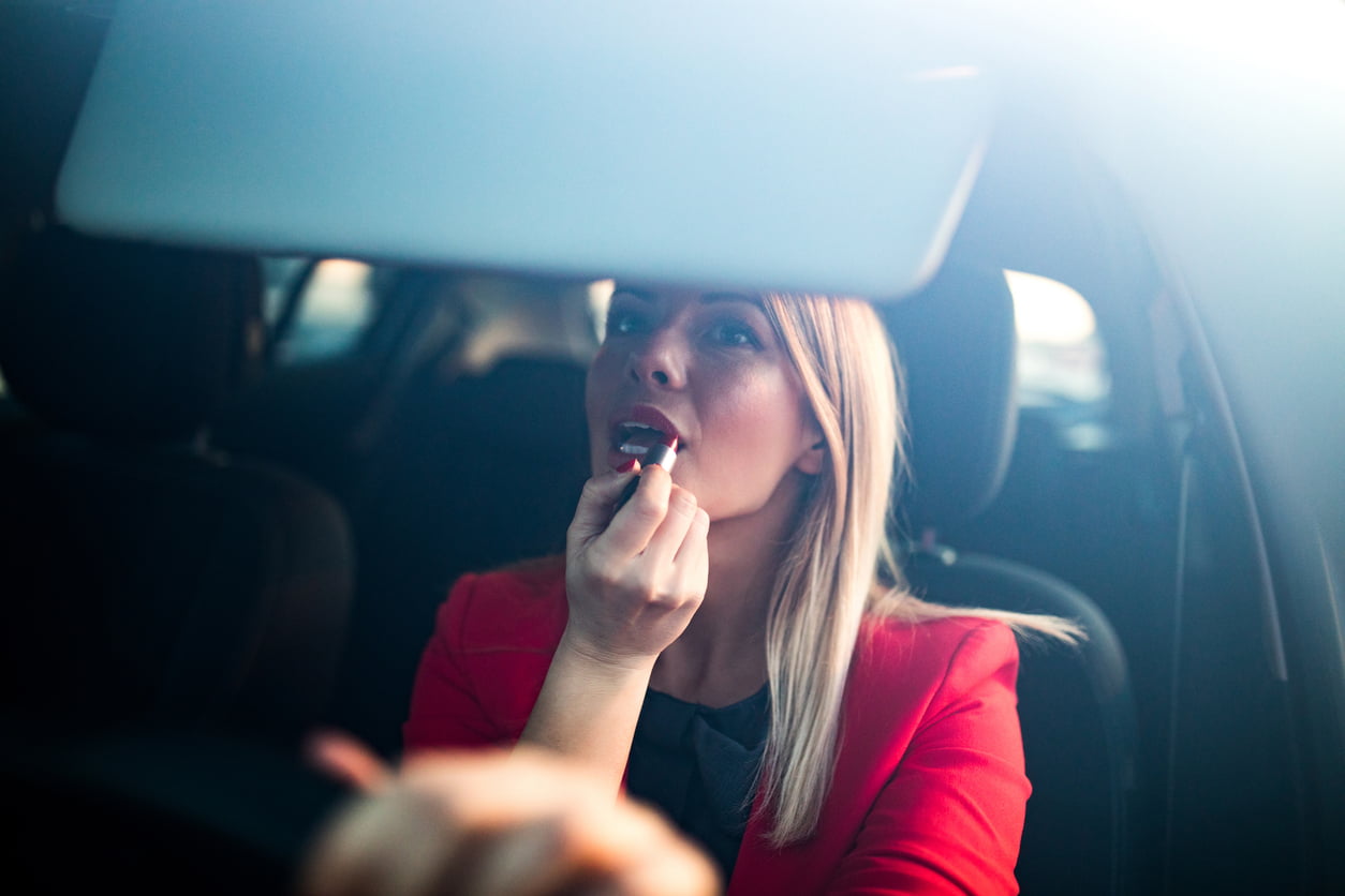 Woman putting a red lipstick while sitting in a car - penalties for distracted driving
