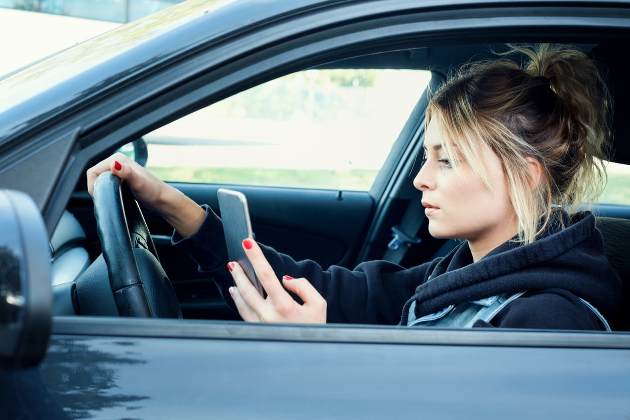 high risk auto insurance - Girl driving car and texting on her smart phone
