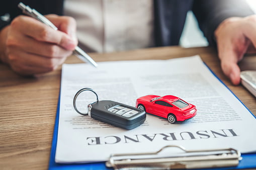 a person filling out an insurance form with a key chain and toy car on top of the paper - FAQs about car insurance