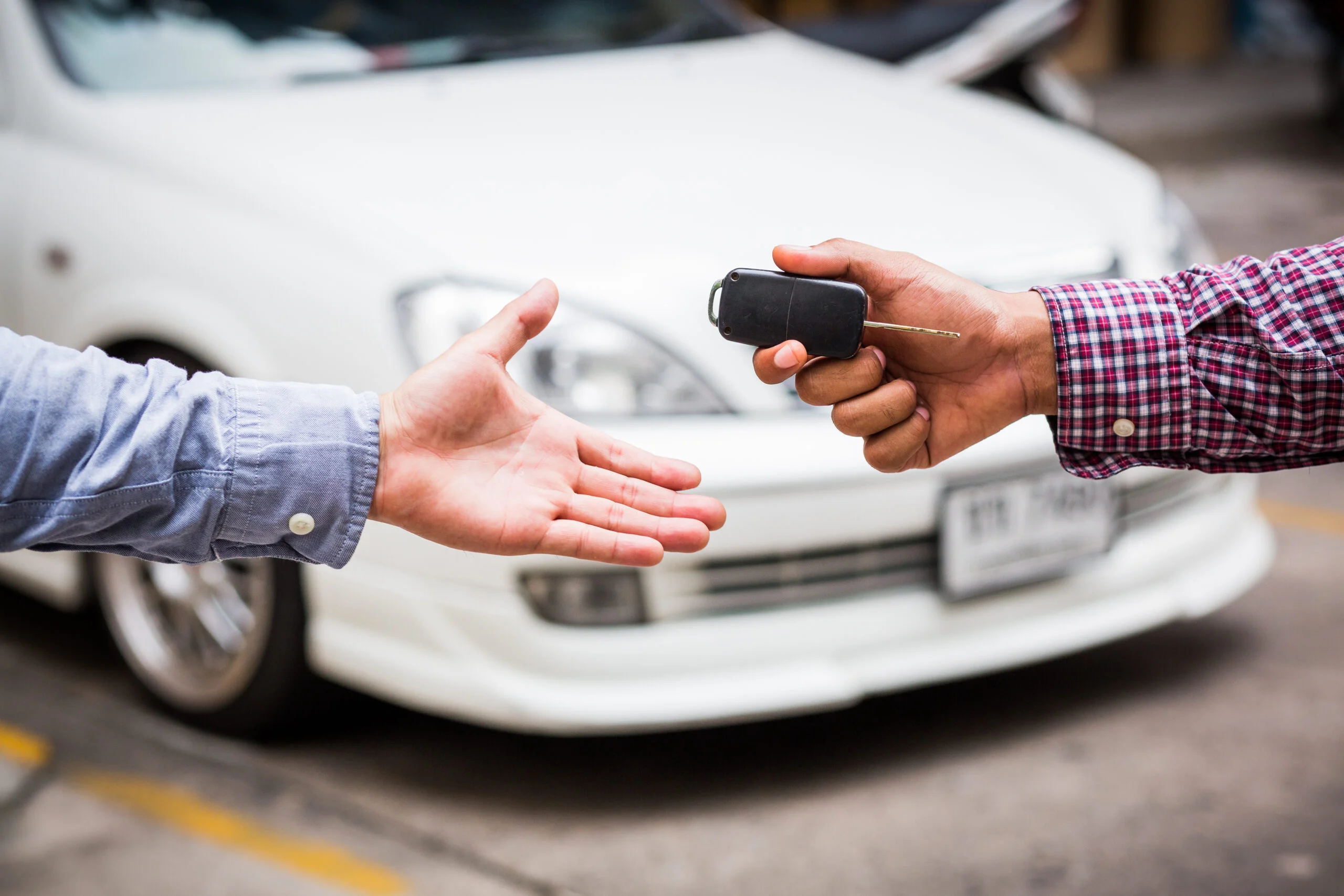 photo of a hand passing keys to another hand in front of a white vehicle - used vehicle information package