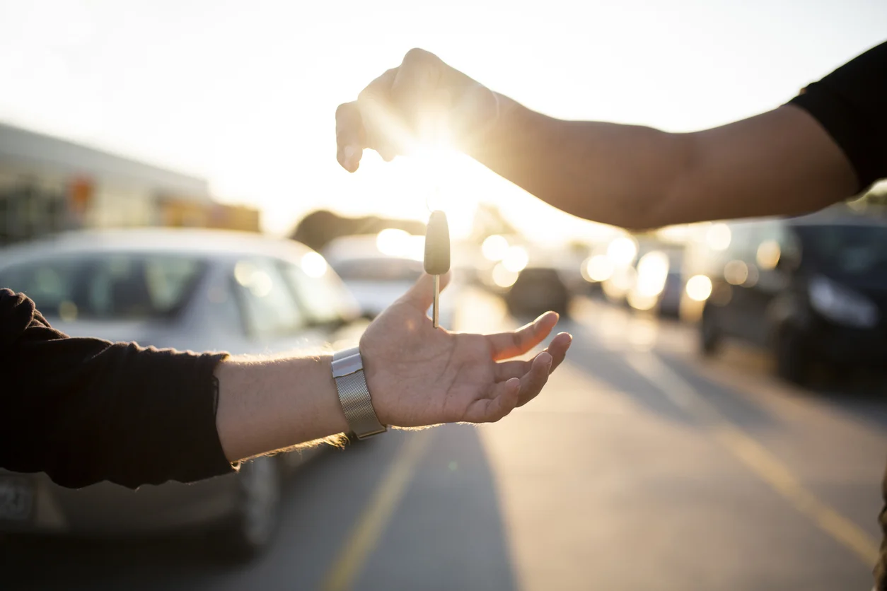 one hand passing car keys to another hand in a parking lot - non-owner car insurance in Ontario
