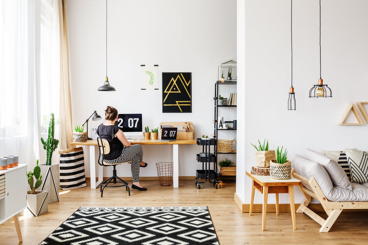 Young girl sitting at desk in a bright, minimalist loft interior with simple white and wooden furniture, sofa, plants, basket, window, paper bag and industrial rack full of unique accessories - what is contents insurance