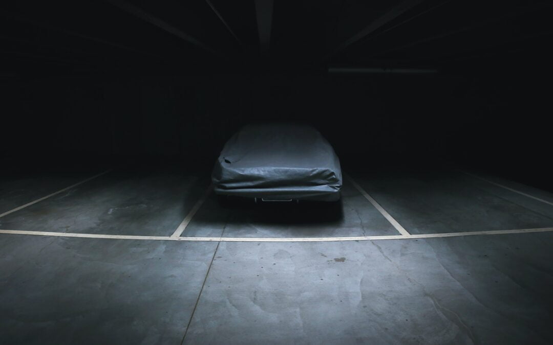 Unused car parked in a dark parking garage with a car cover