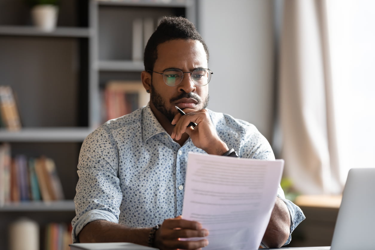 Black male wearing glasses sits at desk holding papers looking perplexed. Home insurance rates in Ontario