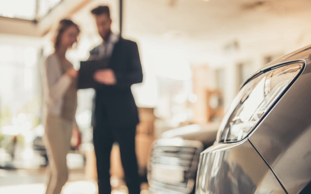 Beautiful young woman is talking to handsome bearded sales manager while choosing a car in dealership - should you lease or finance your vehicle?