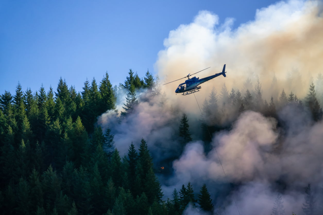 Helicopter fighting BC forest fires during a hot sunny summer day. Taken near Port Alice, Northern Vancouver Island, British Columbia, Canada. - climate change and home insurance
