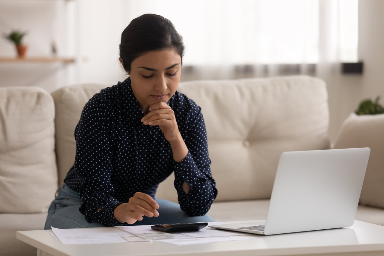 Thoughtful millennial indian lady sit on sofa engaged in paperwork at home calculate expenses planning budget. Young mixed race female homeowner count payable amount before paying utility bills online - auto insurance endorsements