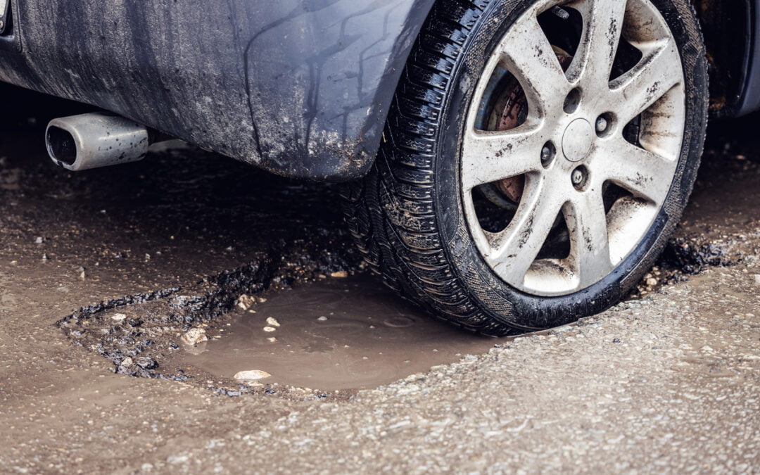 car tire in big pothole on the road - damages caused by potholes