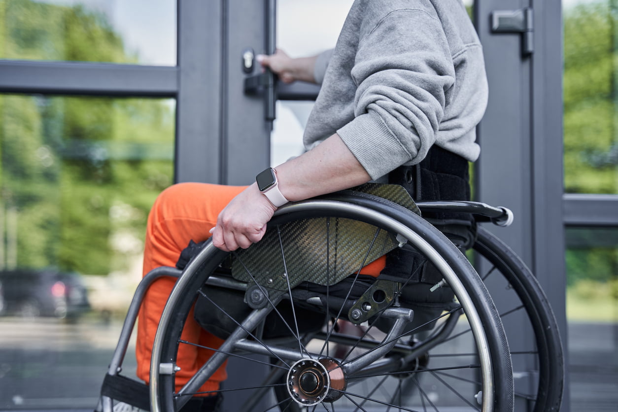 Cropped view of the physically challenged girl moving herself at the wheelchair and opening doors of the building. OCF-19 catastrophic impairment, paralysis as a result of a car accident