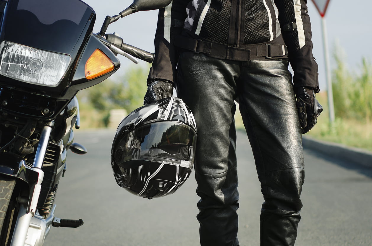 motorcycle coverage - A woman biker holds a protective helmet in her hand, standing next to a motorcycle. Close-up