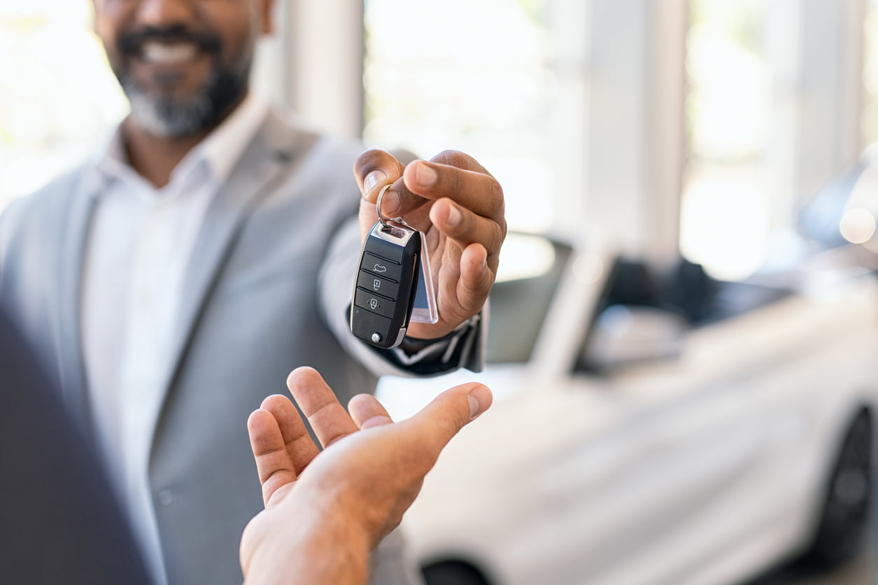 vehicle supply shortage - Closeup hand of cardealer giving new car key to customer. Detail of salesman hand giving keys to a client at showroom. Man's hand receiving car keys from african agent in a auto dealership with copy space.