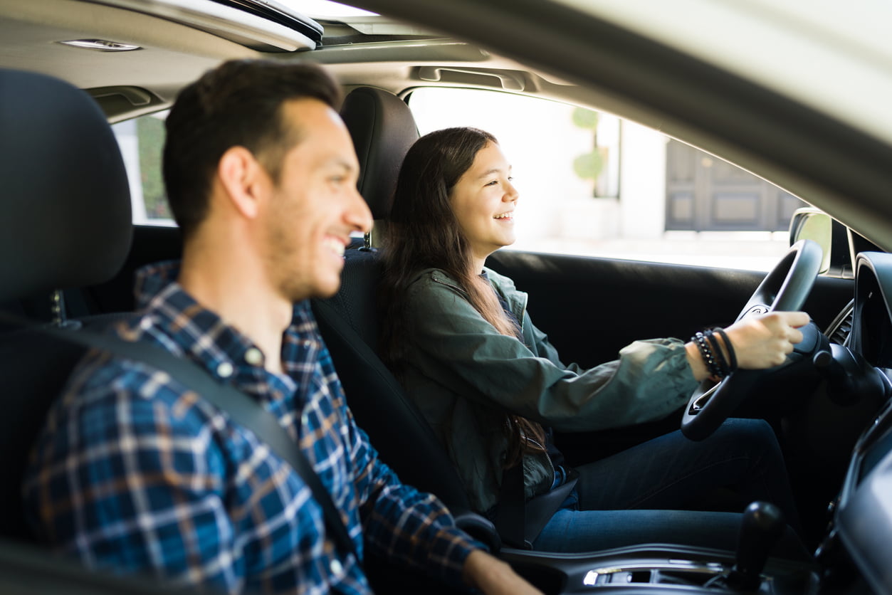 new drivers insurance - Happy handsome dad and teen daughter laughing while driving. Adolescent girl practicing her driving skills with her father