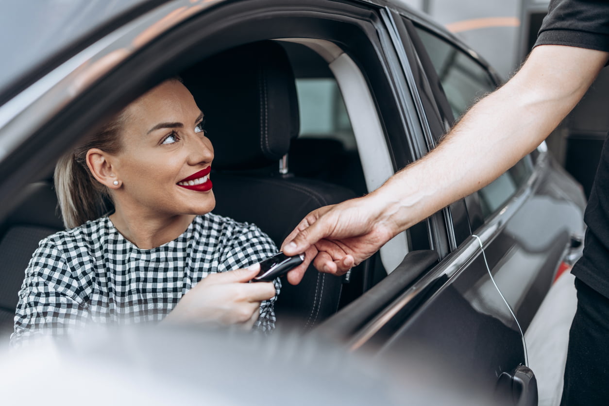 out-of-province vehicle - Satisfied and smiled female buyer sitting in her new car. She is smiling, looking at seller through open window while taking car keys from him