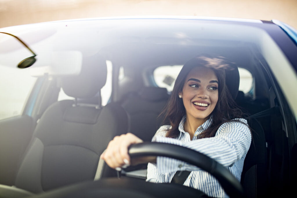 multi-vehicle insurance - Happy woman driving a car and smiling. Cute young success happy brunette woman is driving a car. Portrait of happy female driver steering car with safety belt
