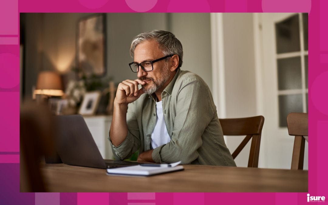 choosing auto insurance deductibles - A focused mature male freelancer sitting at the wooden table at home and reading online projects on a laptop.