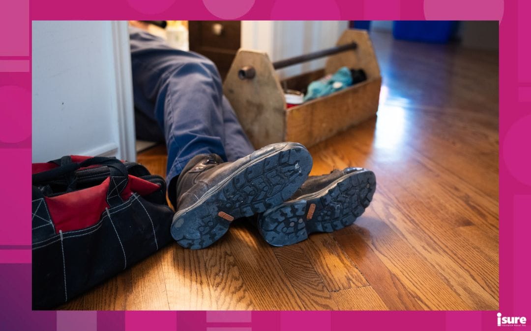 A tradesperson is working on a sink, with his tools beside his feet.
