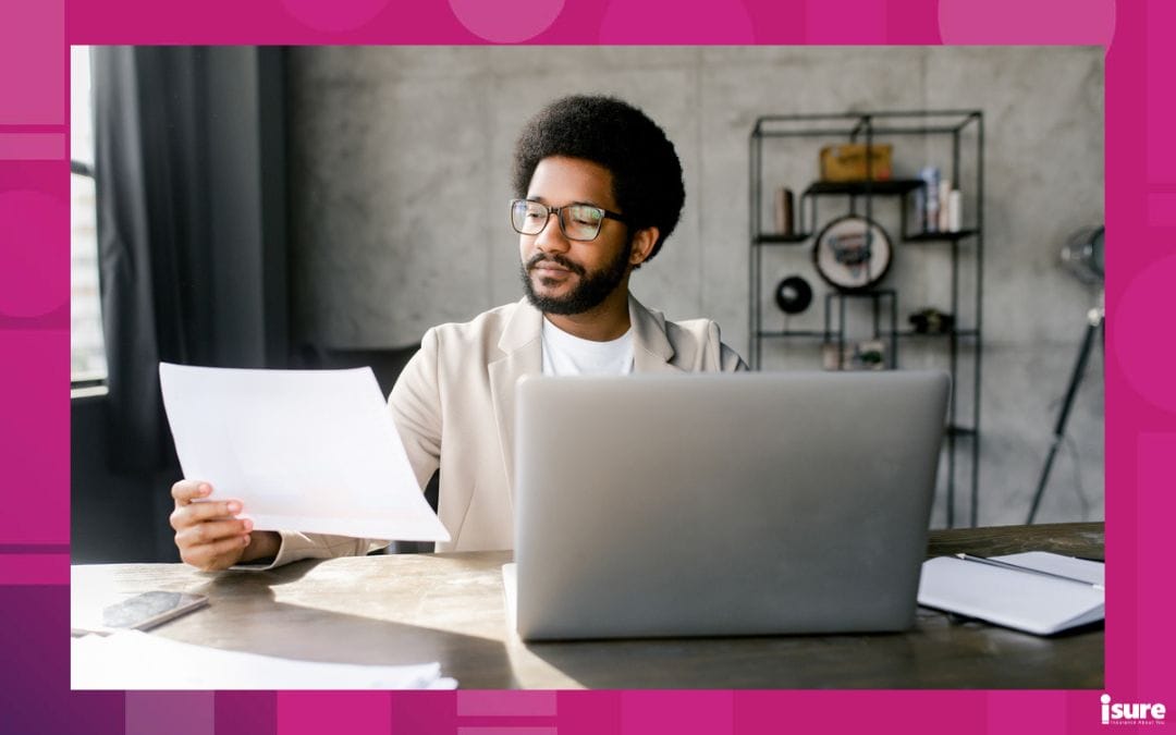underinsured businesses - Young businessman reviewing documents while working on a laptop in an office with an industrial aesthetic. Analytical and contemplative aspects of business management within a modern, urban setting