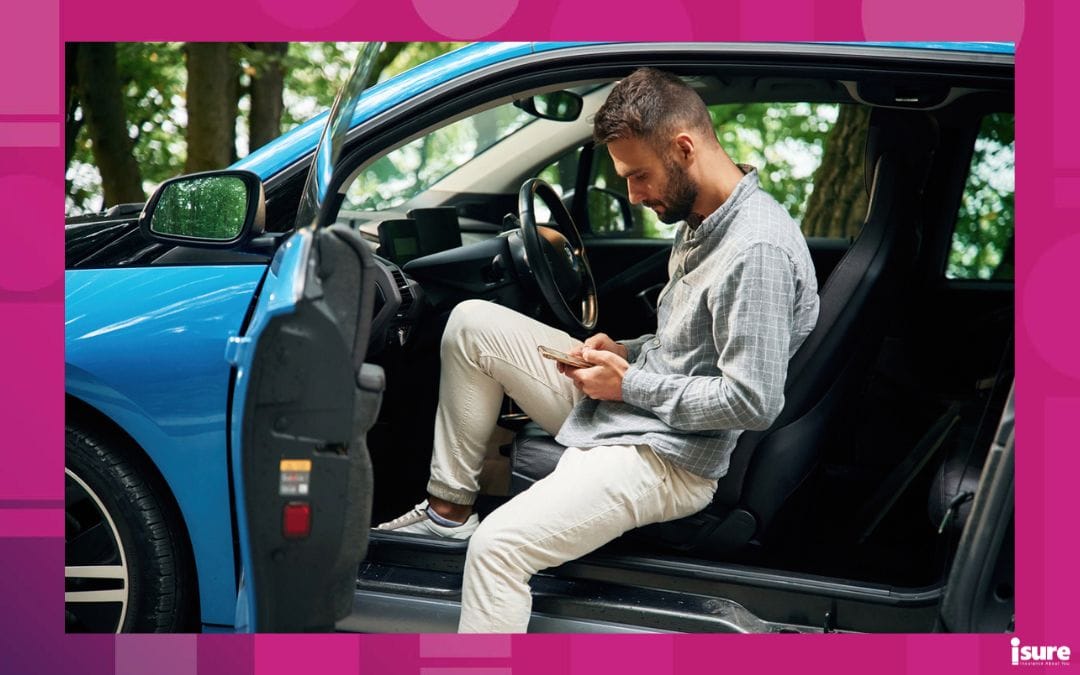 Young man is sitting in his blue car outdoors with the door open, while on his smartphone reading about effects of US tariffs on home and auto insurance