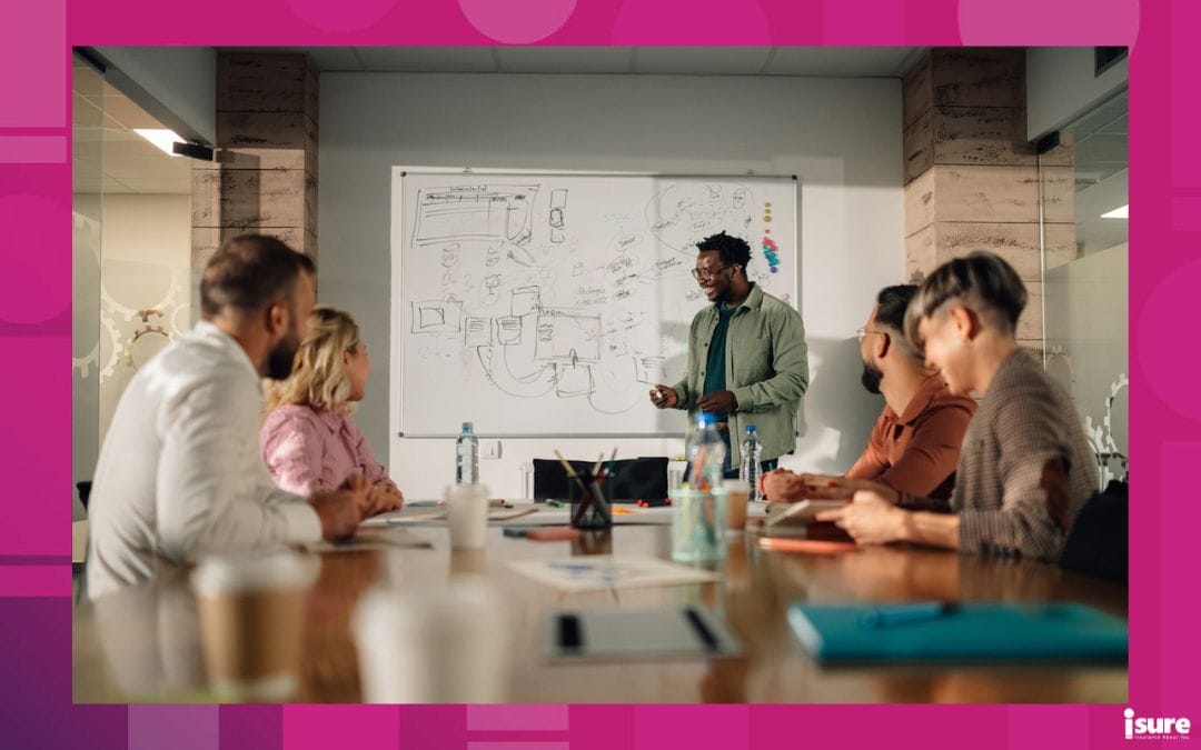 Diverse team of professionals is sitting at a large wooden table in a modern office, attentively listening to an african american businessman presenting a new project on a whiteboard, stressing the importance of startup business insurance in Ontario