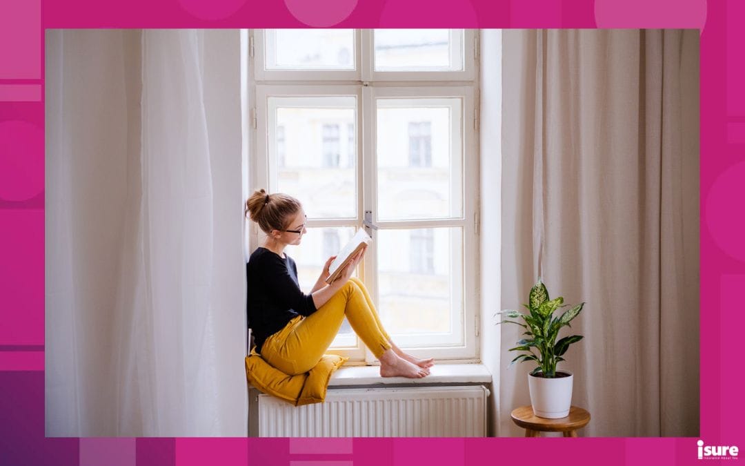 A young happy college female student with a book sitting on window sill at home, studying. Renting without tenant insurance