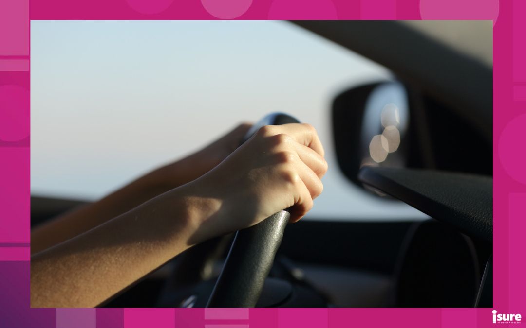 The hands of a young driver grip the steering wheel of a car.